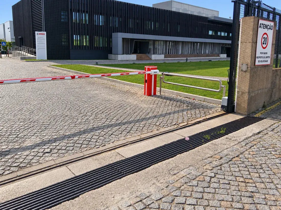 Barreira automática FAAC B680H com haste de luzes LED junto ao portão de entrada de um centro empresarial em Estarreja
