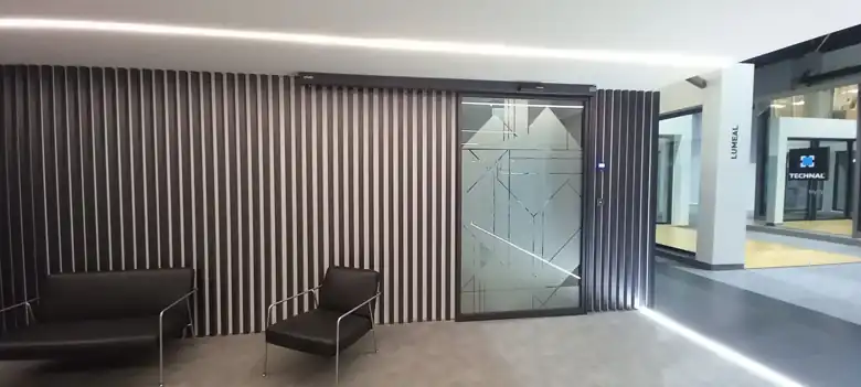Enquadramento da porta automática da sala de formação com o revestimento de ripas e a zona de espera, numa sede empresarial em Loures