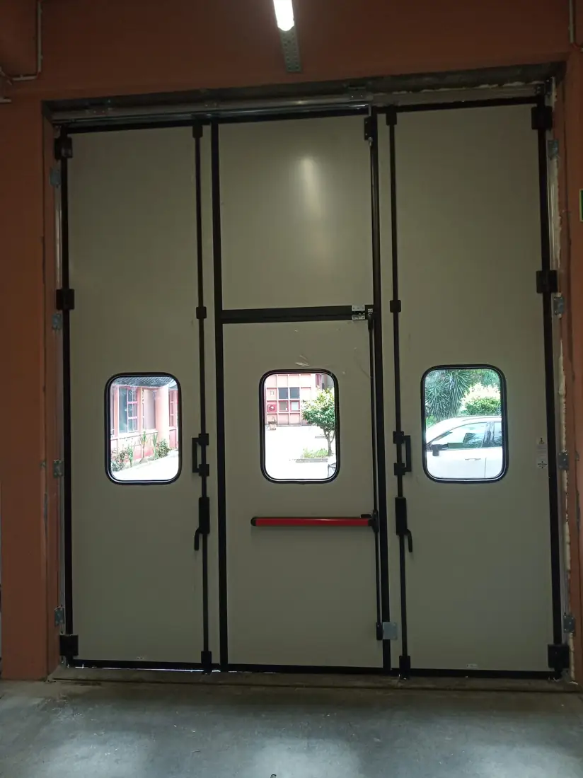 Face interior branco-cinza da porta de harmónio, com barra antipânico na porta de serviço
