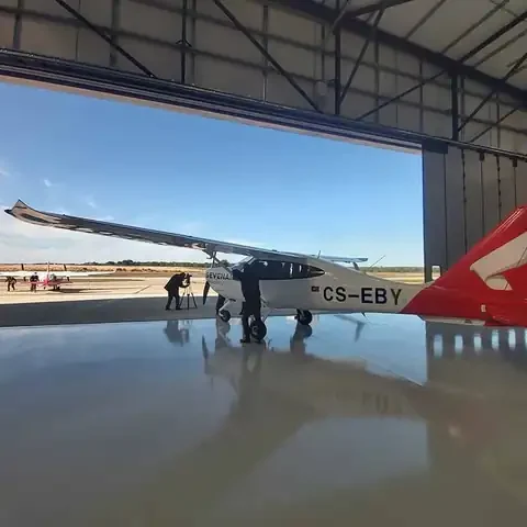 Avião dentro do hangar do Aeródromo Municipal de Ponte de Sôr, com a porta de harmónio aberta ao fundo, a mostrar a dimensão do vão