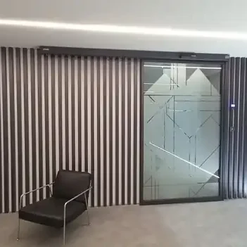 Enquadramento da porta automática da sala de formação com o revestimento de ripas e a zona de espera, na sede da Hydro